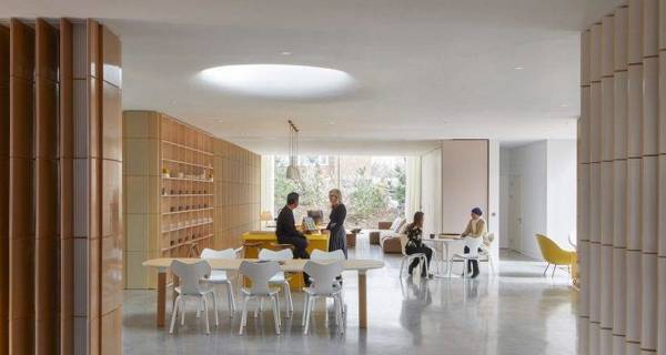 Interior of Maggie’s Southampton featuring a central kitchen with four bespoke ceramic block walls, high glass partitions, sliding doors, and stainless steel panels with a ripple effect.