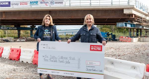 Two women stand together holding a large cheque for the Strong Foundations grant, smiling for the camera