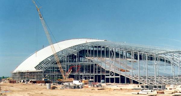 Cranes lifting and positioning curved steel beams to form the distinctive roof of the ski slope.