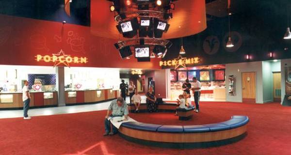 Large open cinema lobby area with signage, seating, and people walking.